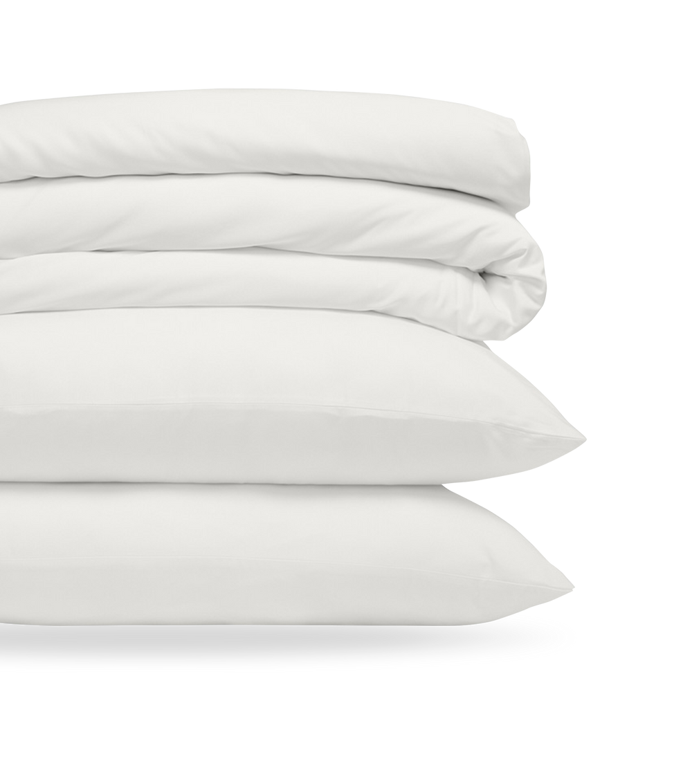 Stack of folded white bedding including pillows and a comforter, neatly arranged to showcase softness and cleanliness.