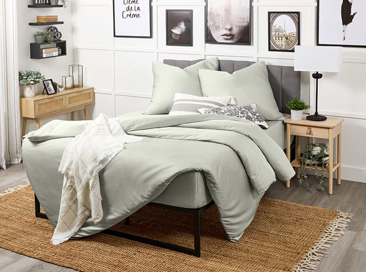 Neatly made bed with light grey bedding in a bedroom setting.