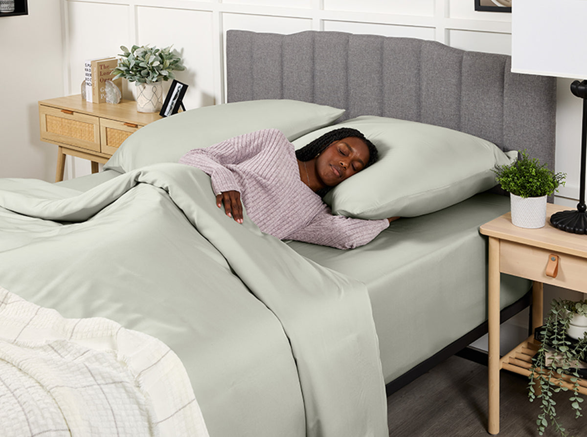 Woman sleeping in a bed with light grey bedding and gray headboard.